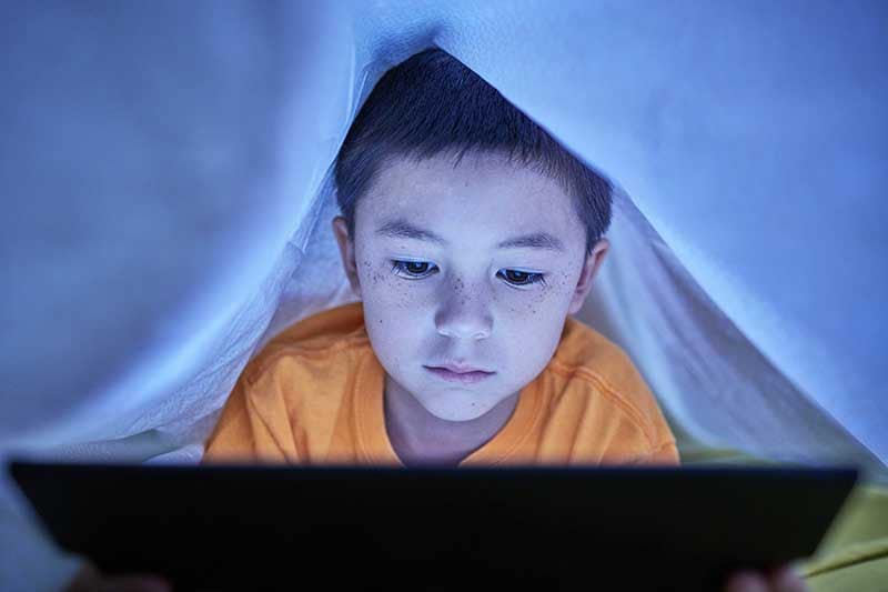 Young boy looking online under the covers