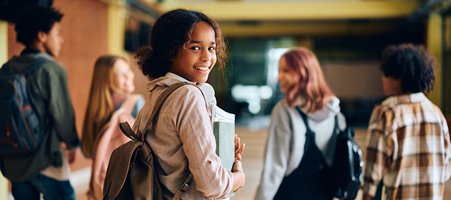 Teen girl walking in school hallway, looking back at camera