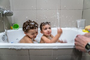 Two toddlers play in the tub while parent stays within arm’s reach to prevent drowning in the bath.