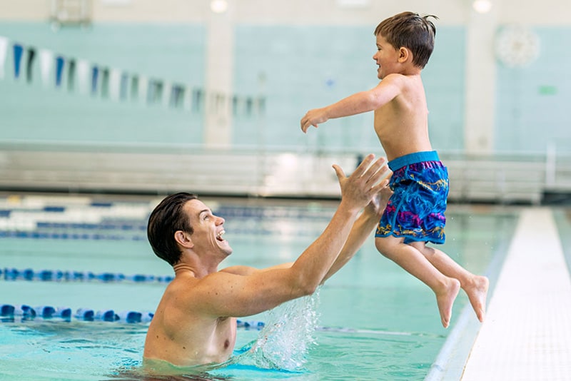 Dad catches toddler as he jumps into the pool during swim lessons. 