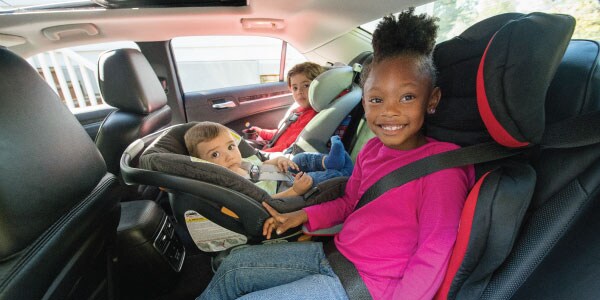 3 children share the back seat in a rear-facing and 2 forward-facing car seats.