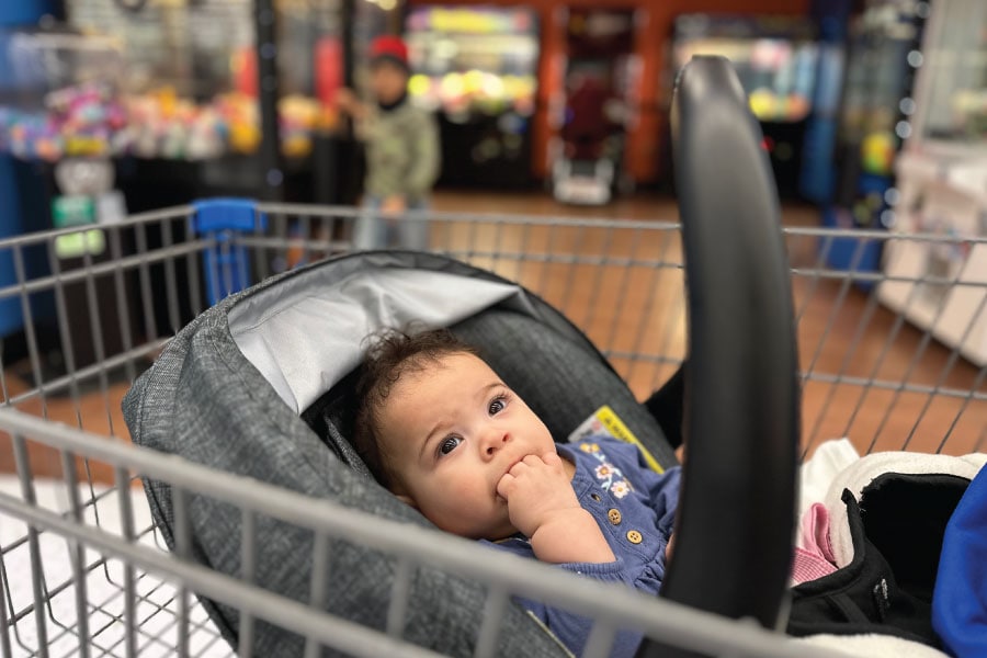 A baby girl rides safely in the basket of a shopping cart.