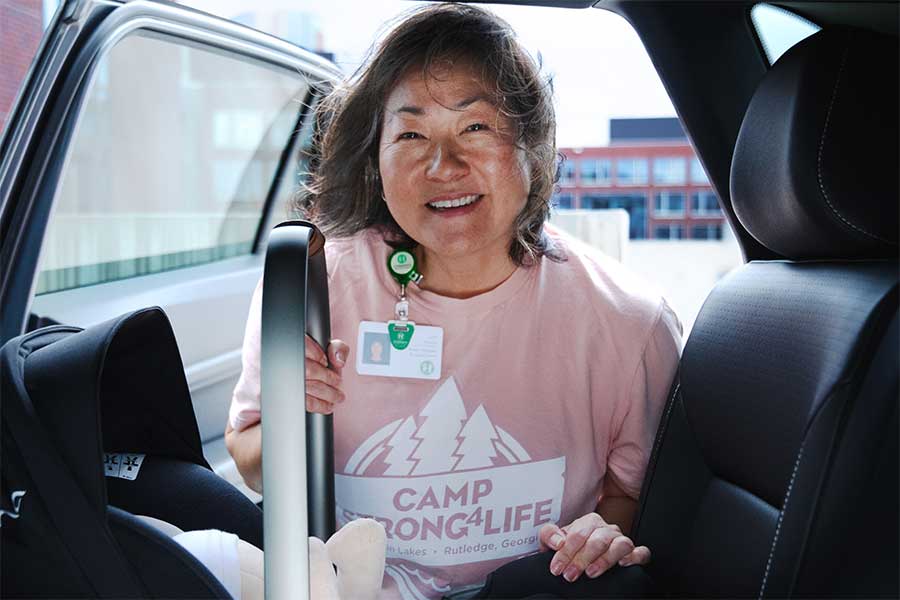 A certified CPST demonstrating how to properly install a rear-facing car seat while smiling at the camera.