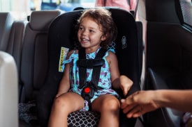 A young girl sits in a forward-facing car seat in the back seat of a vehicle