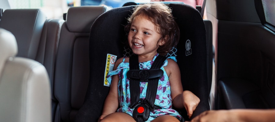A young girl sits in a forward-facing car seat in the back seat of a vehicle