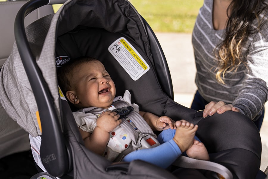 Mom securing crying infant into car seat