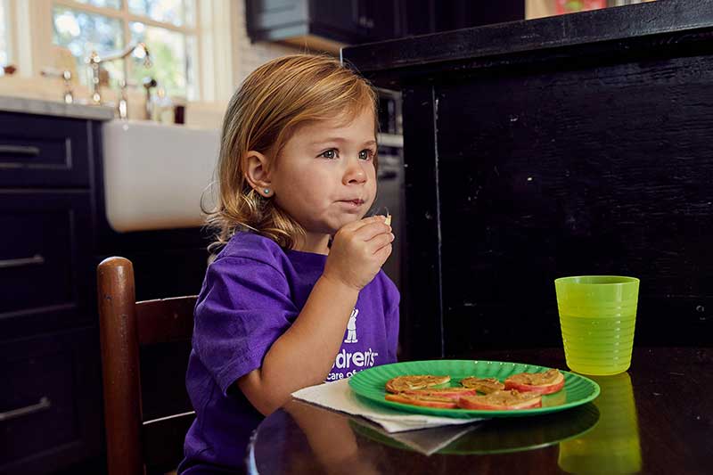 toddler eating thin apple slices with sunflower seed butter