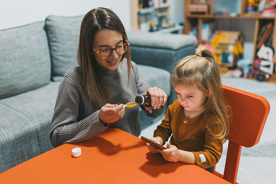 Mom pouring out liquid medicine using a measuring spoon for her child