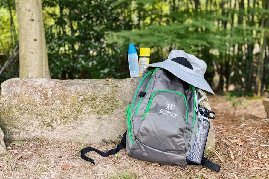 A backpack and hiking gear are shown outside, including bug spray, water, a hat and sunscreen.