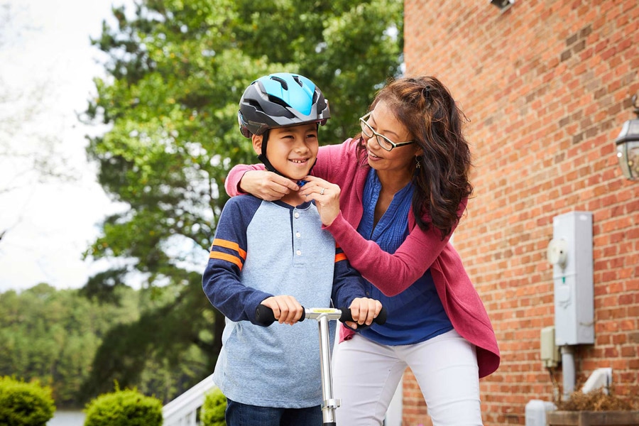 mom putting helmet on son in driveway