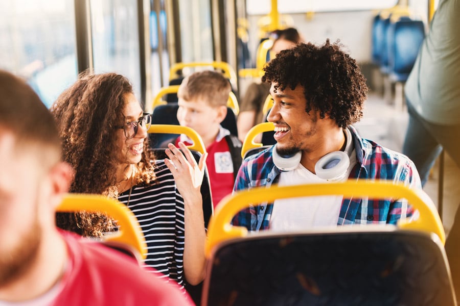 Two teens sit next to each other and talk while riding public transit.