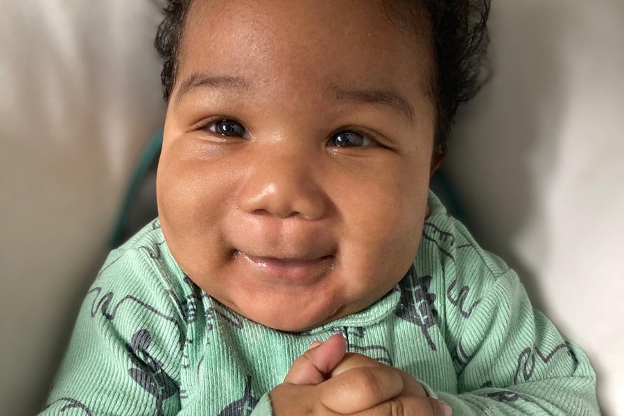 Khyree Kruz Long smiles with his hands folded, wearing a mint green onesie.