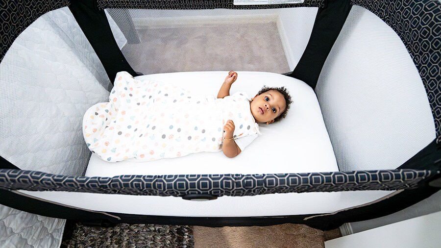A photo of a baby sleeping in a pop-up crib in a fleece sleep sack. 