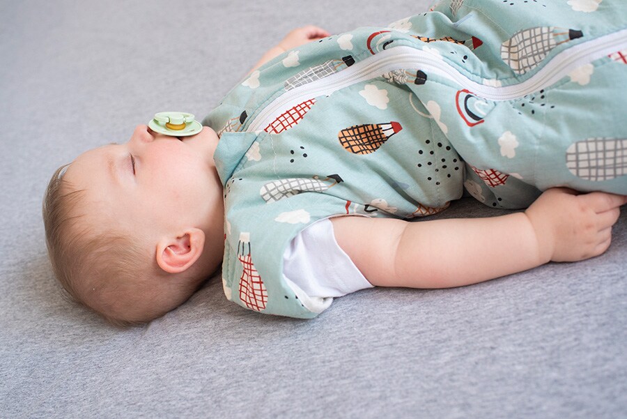 A photo of a baby sleeping safely in a sleep sack with a pacifier. 