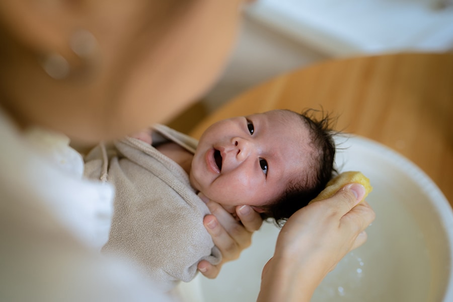Parent holds baby, showing how to sponge bathe a newborn.