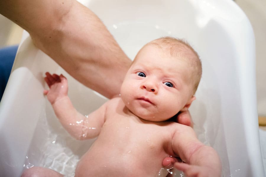 Parent practices baby bath safety by always keeping a hand on baby in the tub.