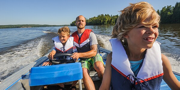 Photo of a dad practicing boat safety with his kids while wearing life vests.