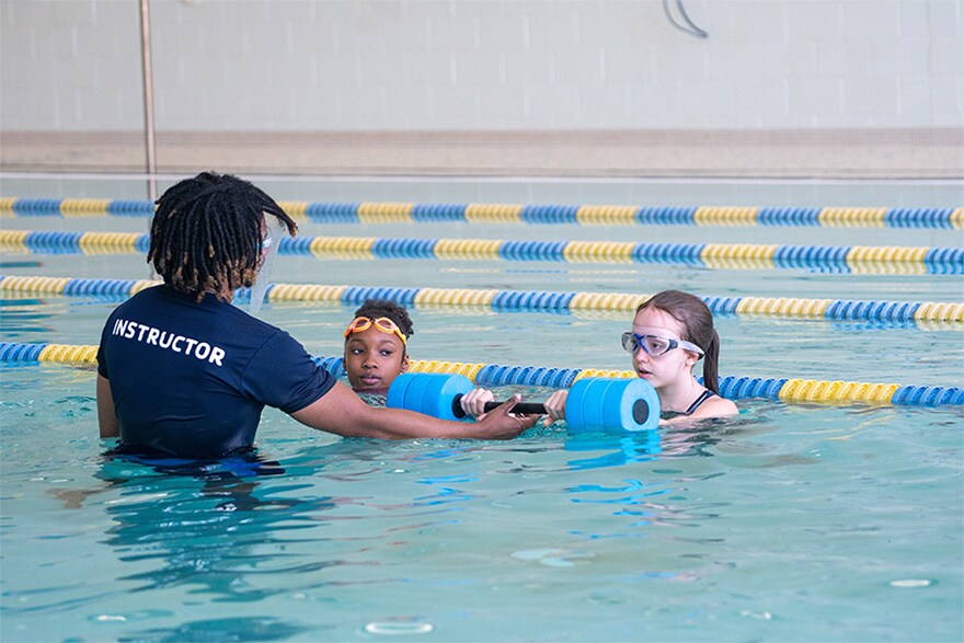 A photo of a certified instructor teaching two kids swimming lessons in indoor pool.