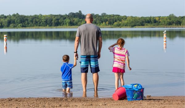 A dad holding his kids hands on the lake shore.