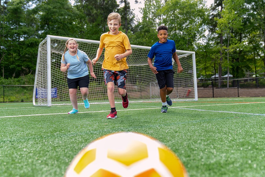 Grade-schoolers smile while chasing a soccer ball, having fun being physically active