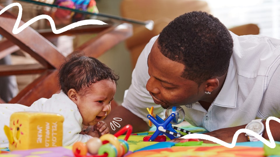 Infant cries during tummy time while dad provides comfort
