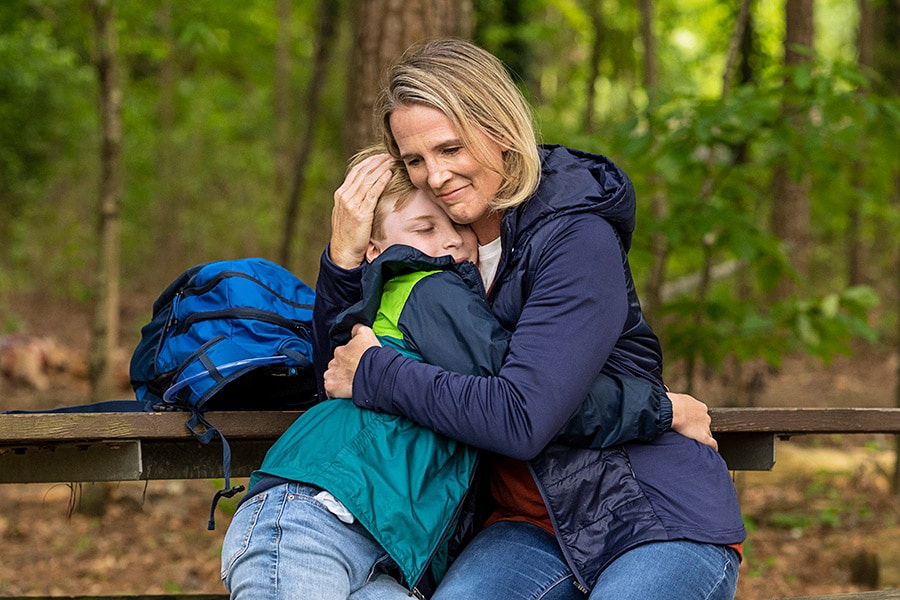 Mom and preteen son hugging on a hiking trail