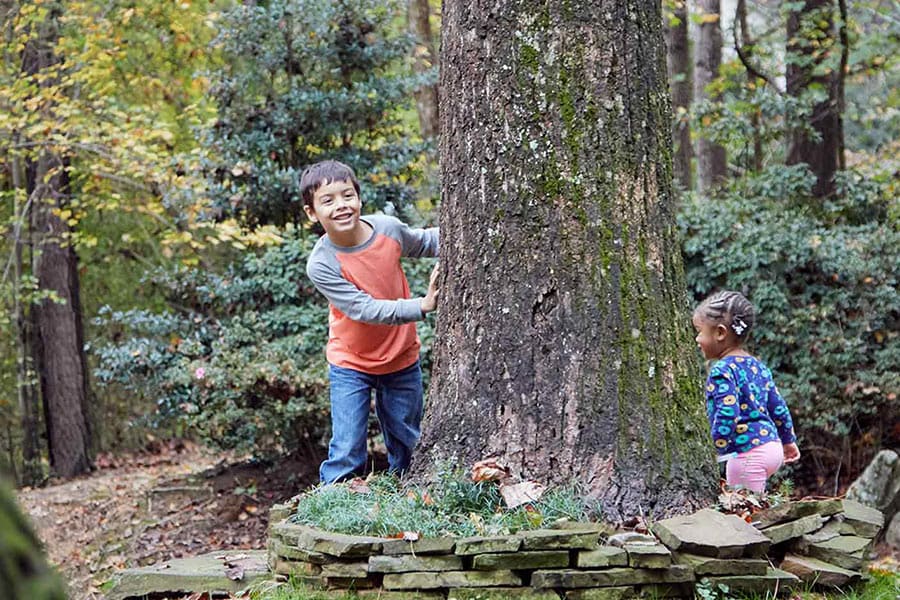 Two kids playing outside in a wooded area