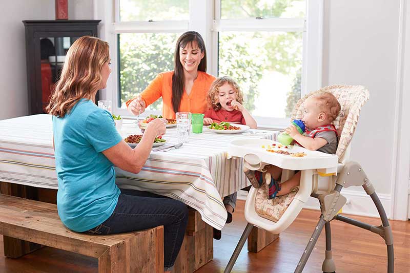 Dos madres comiendo en la mesa con un bebé y un niño.