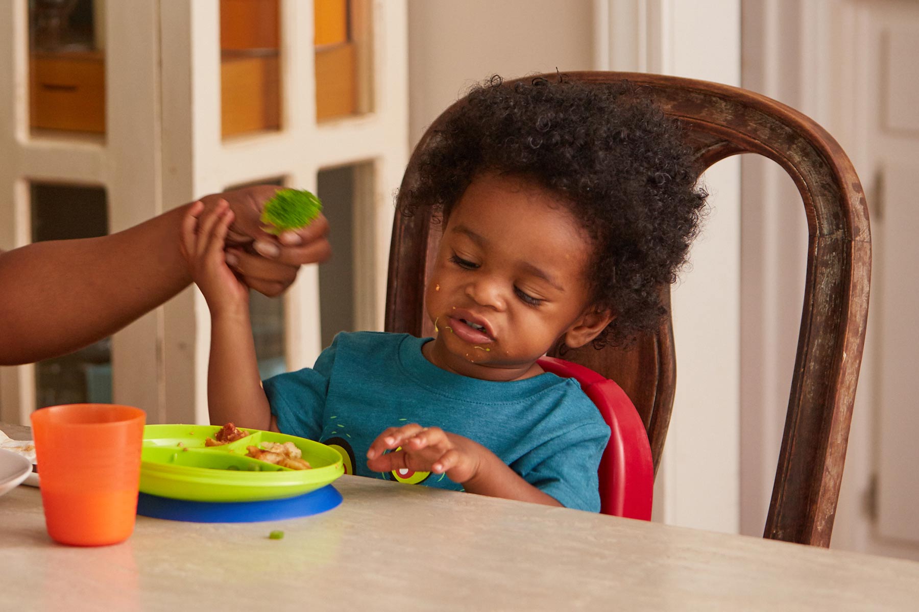 Niño pequeño comiendo en la mesa con sus manos.