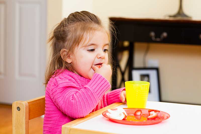 Una niña comiendo alimento sólido con sus dedos.