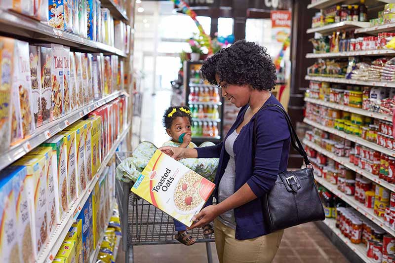 Mujer en el supermercado sujetando una caja de cereal junto a una niña pequeña.