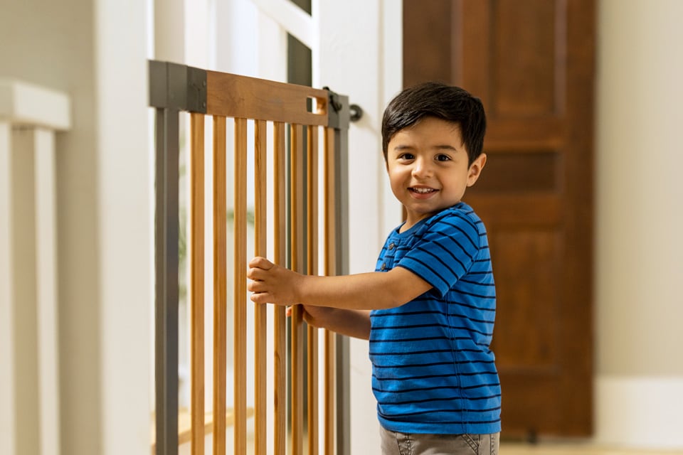 Toddler holding onto baby gate bars near stairs