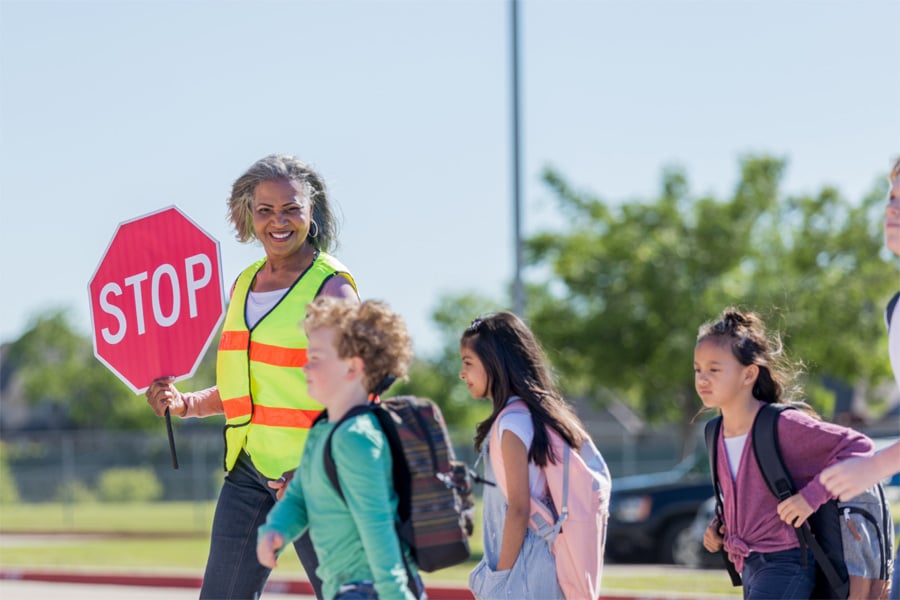 Crossing guard helps three school-age children cross the street.